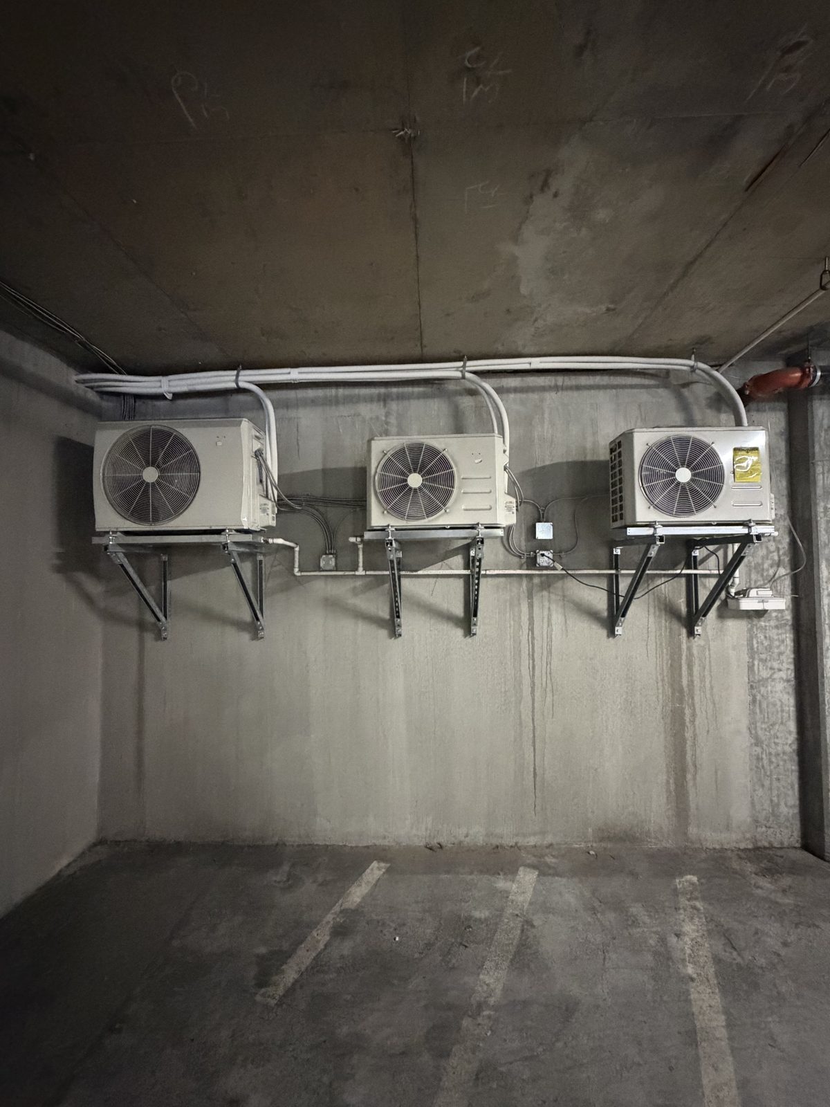 Three mini-split condensers wall-mounted in a parking garage
